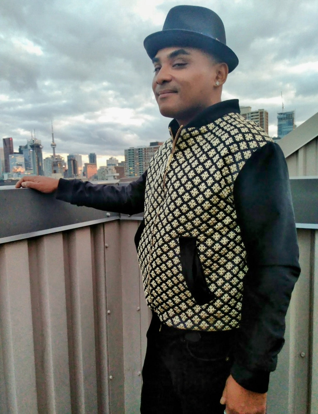 Male model wearing black and gold brocade bomber jacket in front of the Toronto skyline.