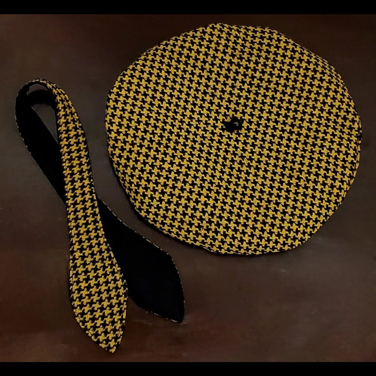 Yellow and black houndstooth beret and matching scarf on brown background