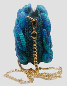 Side view of variegated blue and teal 3D Floral crochet handbag and gold chain strap.