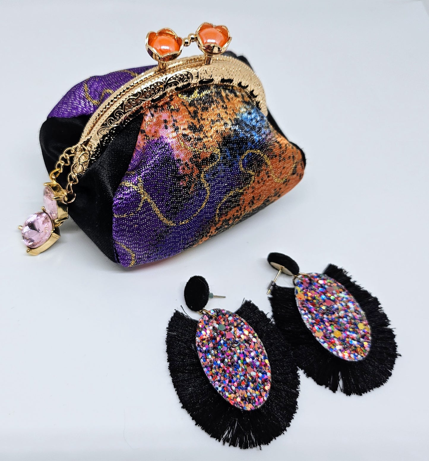 Top view of earrings with Metallic rainbow splash print kiss clasp coin purse with pink jewel charm