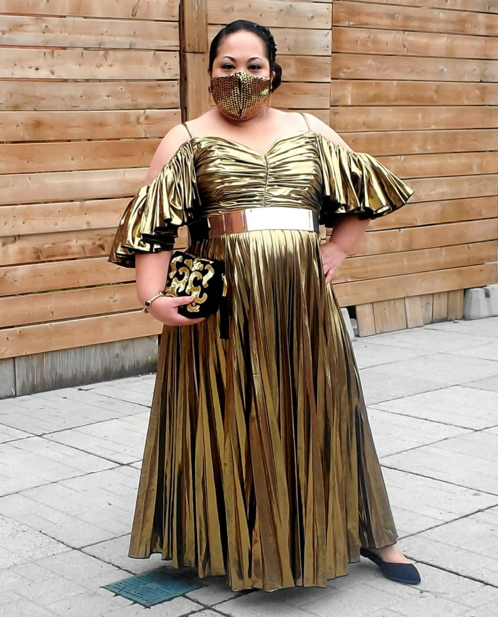 Model in a gold Lamé gown standing in front of a wooden wall