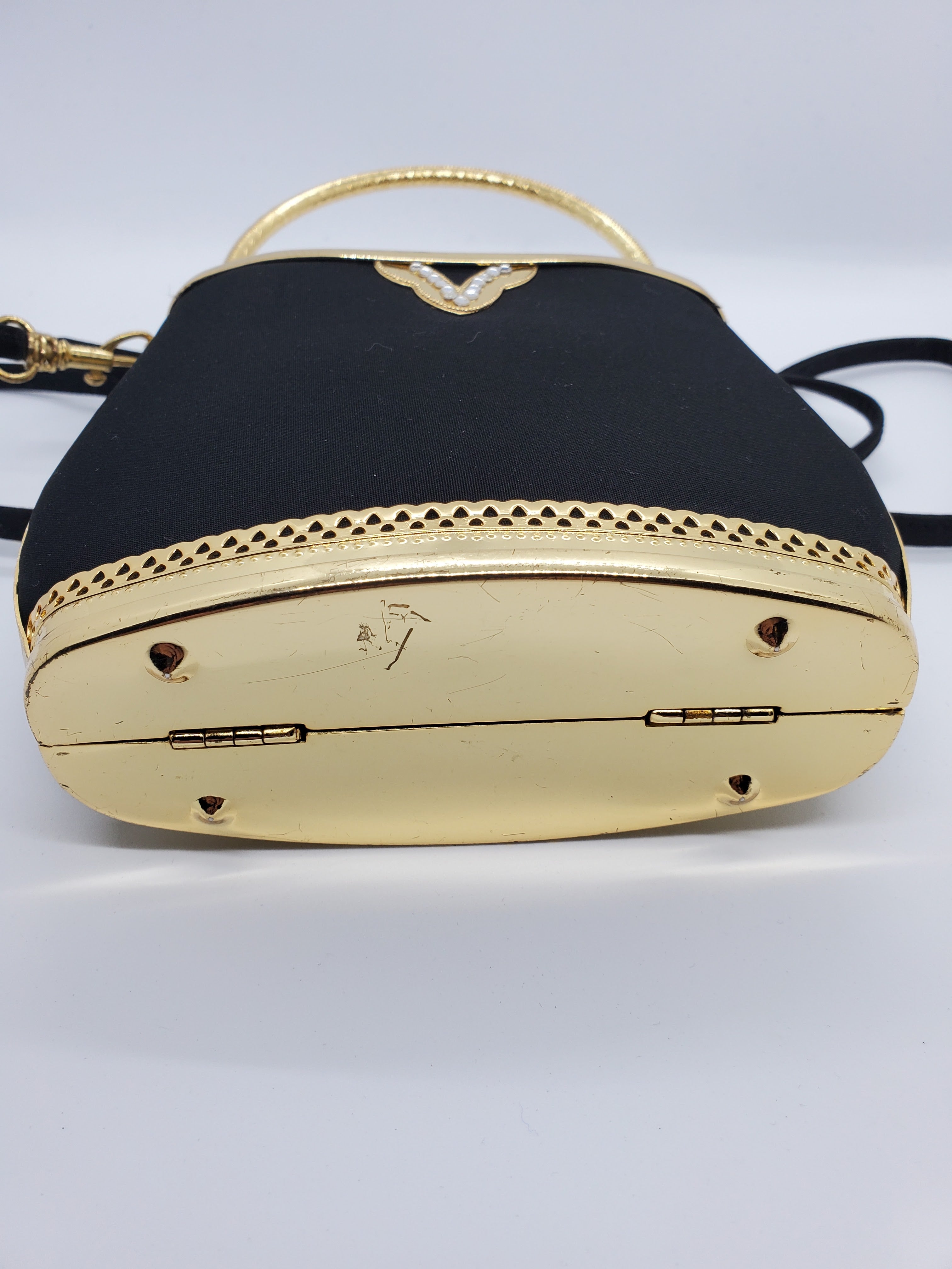 Bottom view of Smooth black handbag with ornate gold frame and handle with rhinestone accents and crossbody strap
