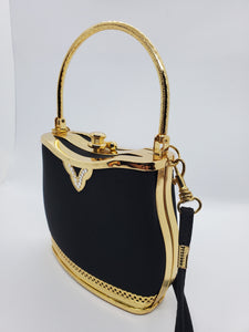 Side view of Smooth black handbag with ornate gold frame and handle with rhinestone accents and crossbody strap