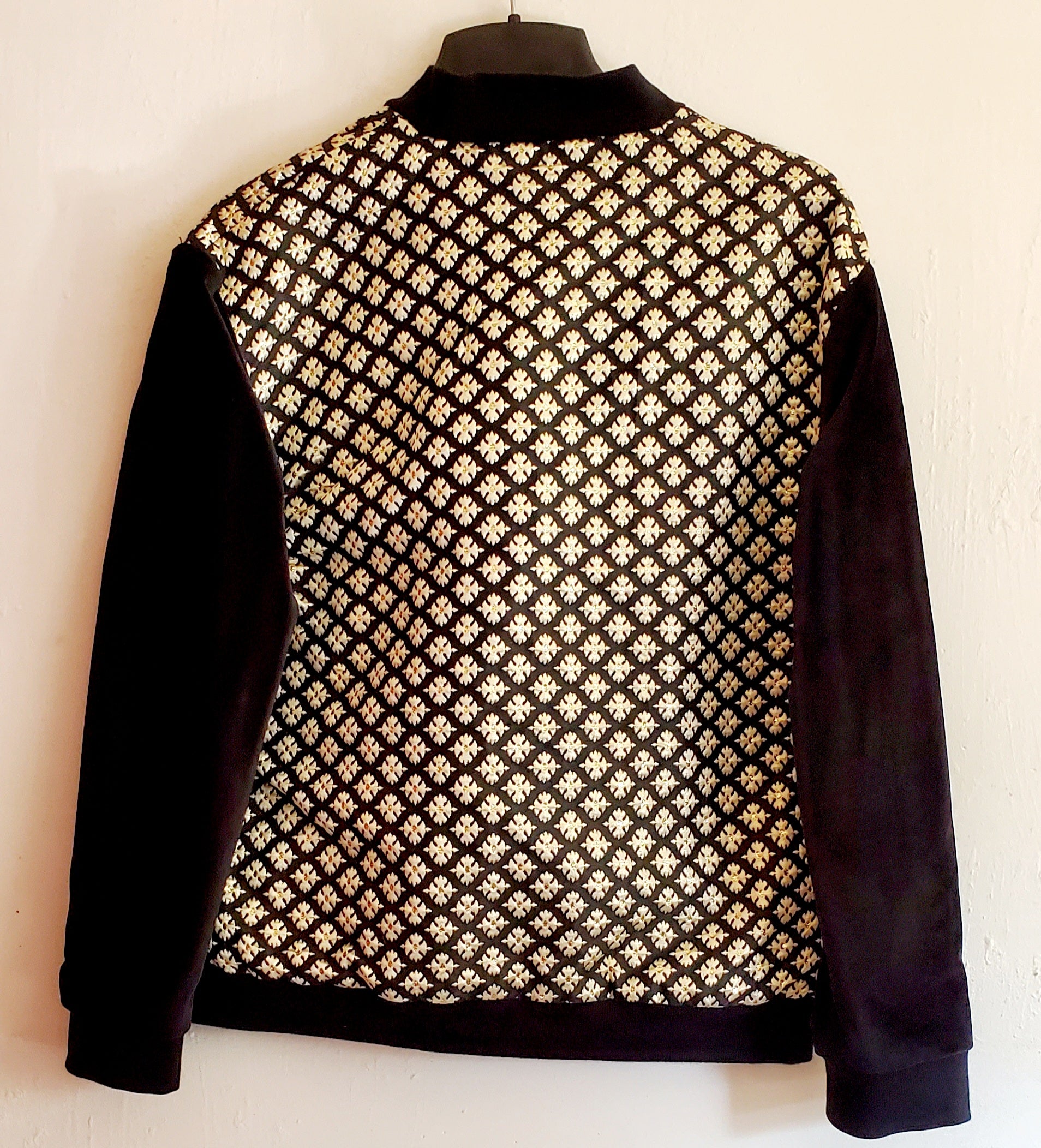 Back view of black and gold brocade bomber jacket on white background.
