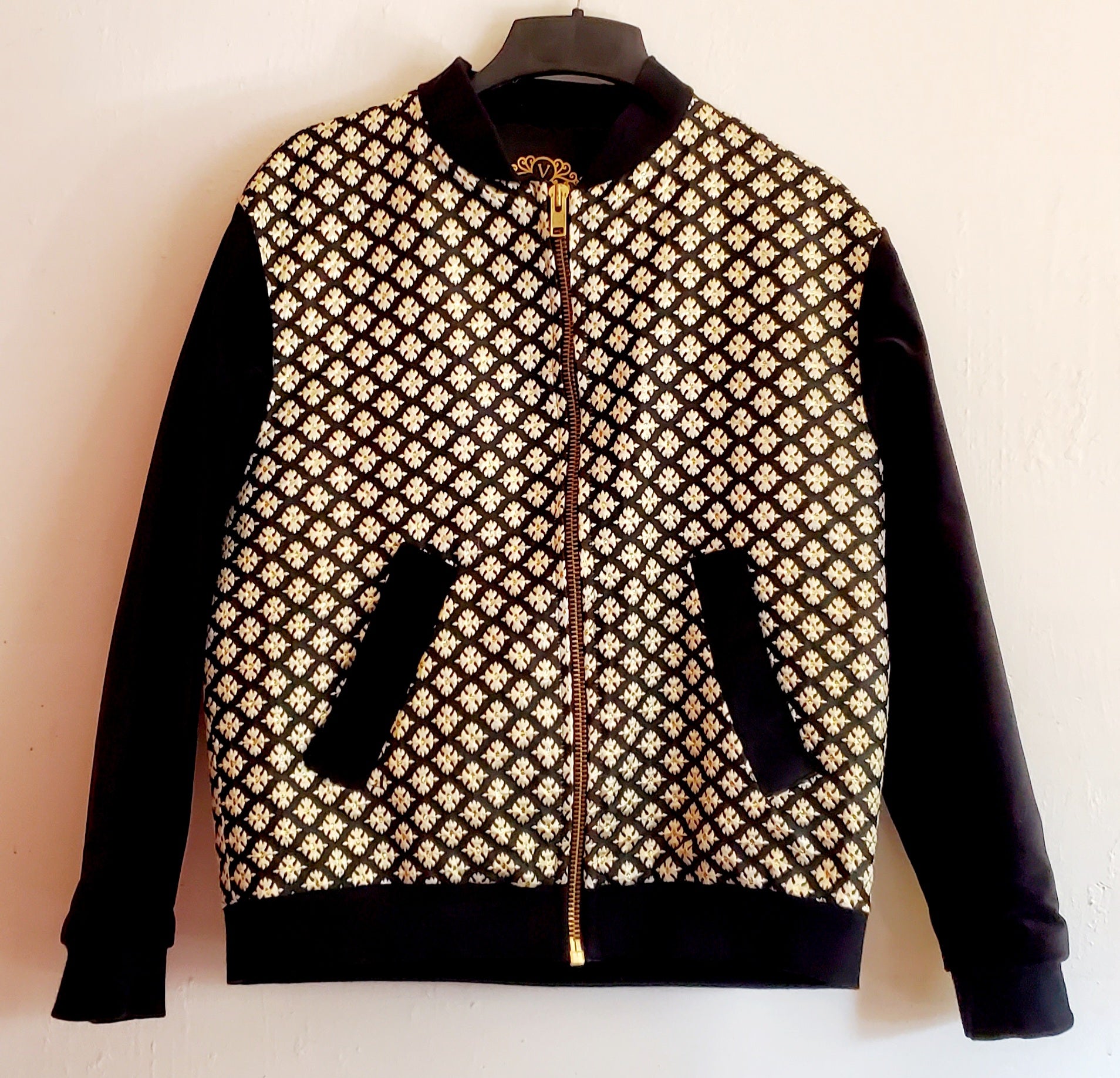 Front view of black and gold brocade bomber jacket on white background.