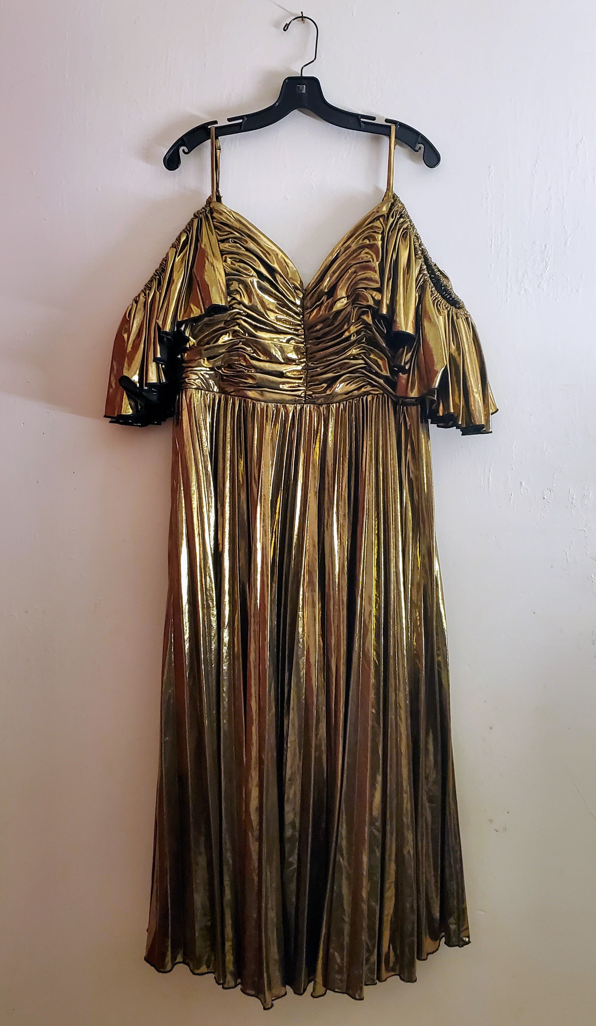 Gold pleated Lamé dress with ruched bodice and off the shoulder ruffled sleeves hanging on  white background.