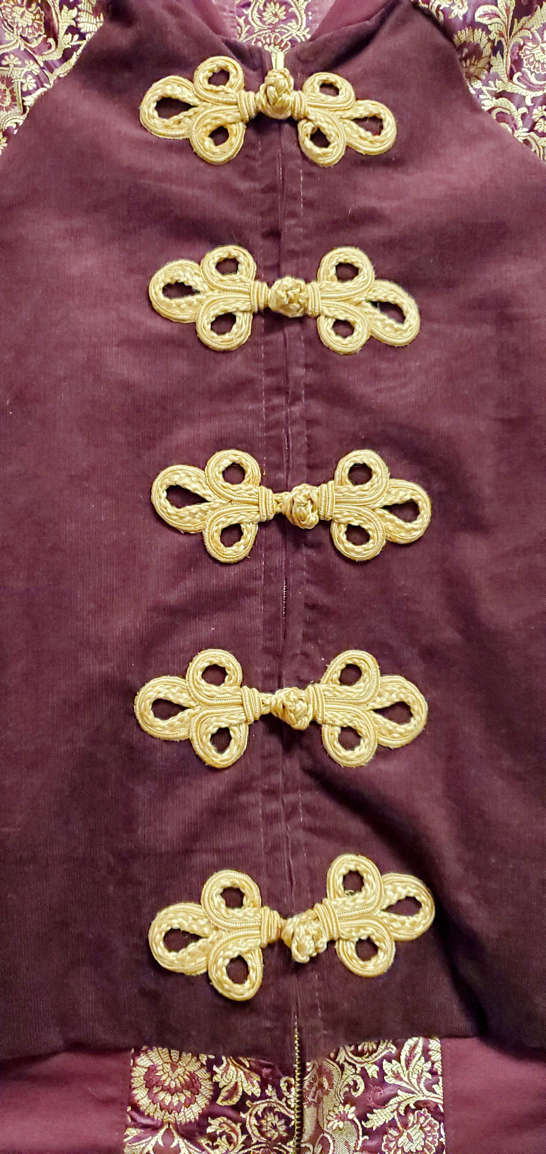 close up front view of Burgundy corduroy bomber jacket with metallic gold sleeve and knot closures