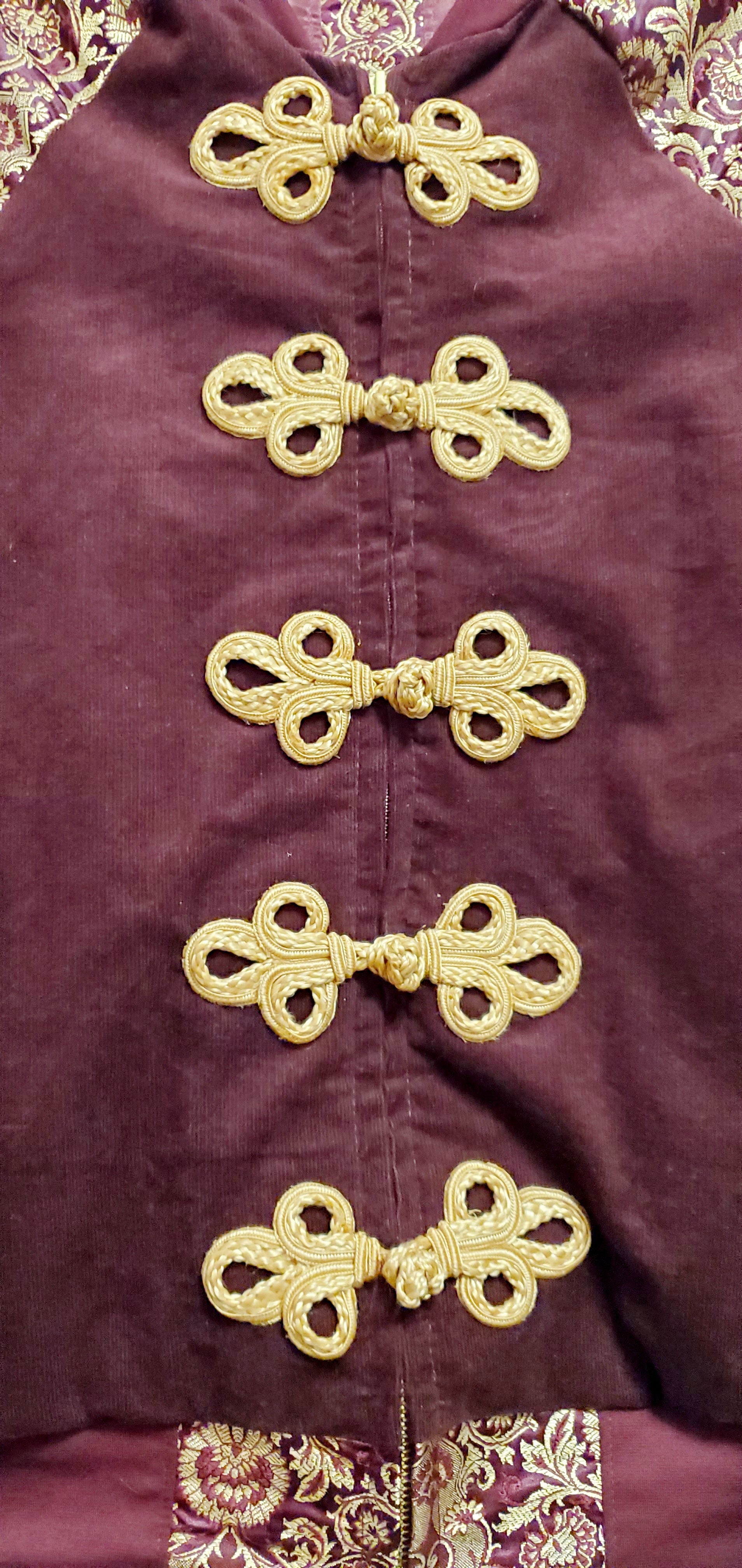 close up front view of Burgundy corduroy bomber jacket with metallic gold sleeve and knot closures