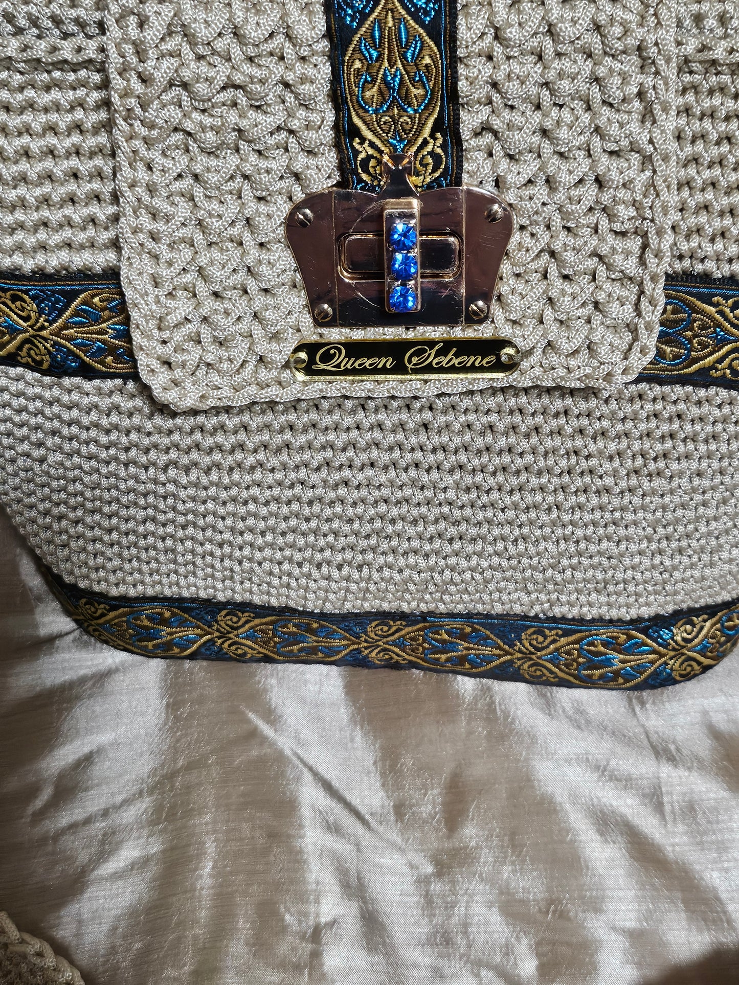 Close up Front view of Cream coloured crochet handbag with Teal and Gold paisley trim