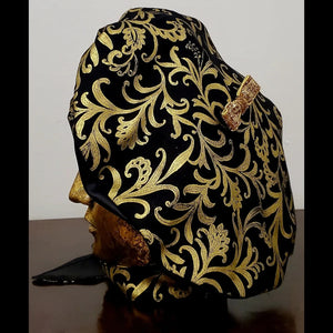Side view. Black and gold damask printed beret with bow detail and matching scarf on mannequin head