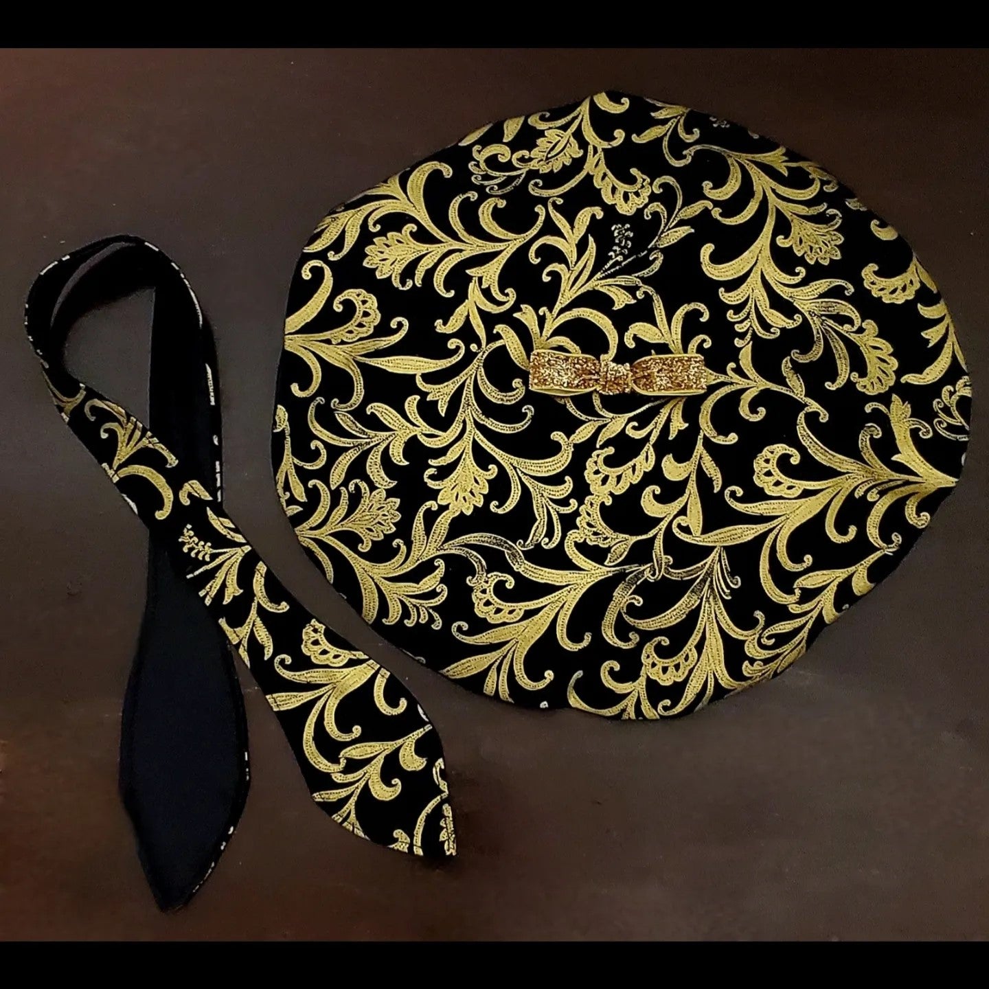Black and gold damask printed beret with bow detail and matching scarf on brown background