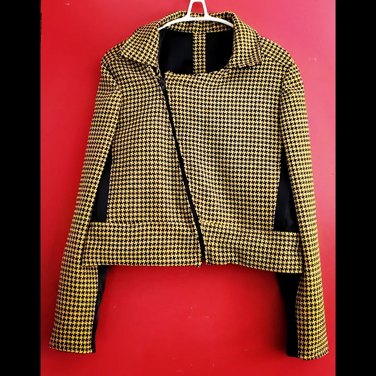 Front view of fully zipped yellow and black houndstooth cropped moto jacket on red background