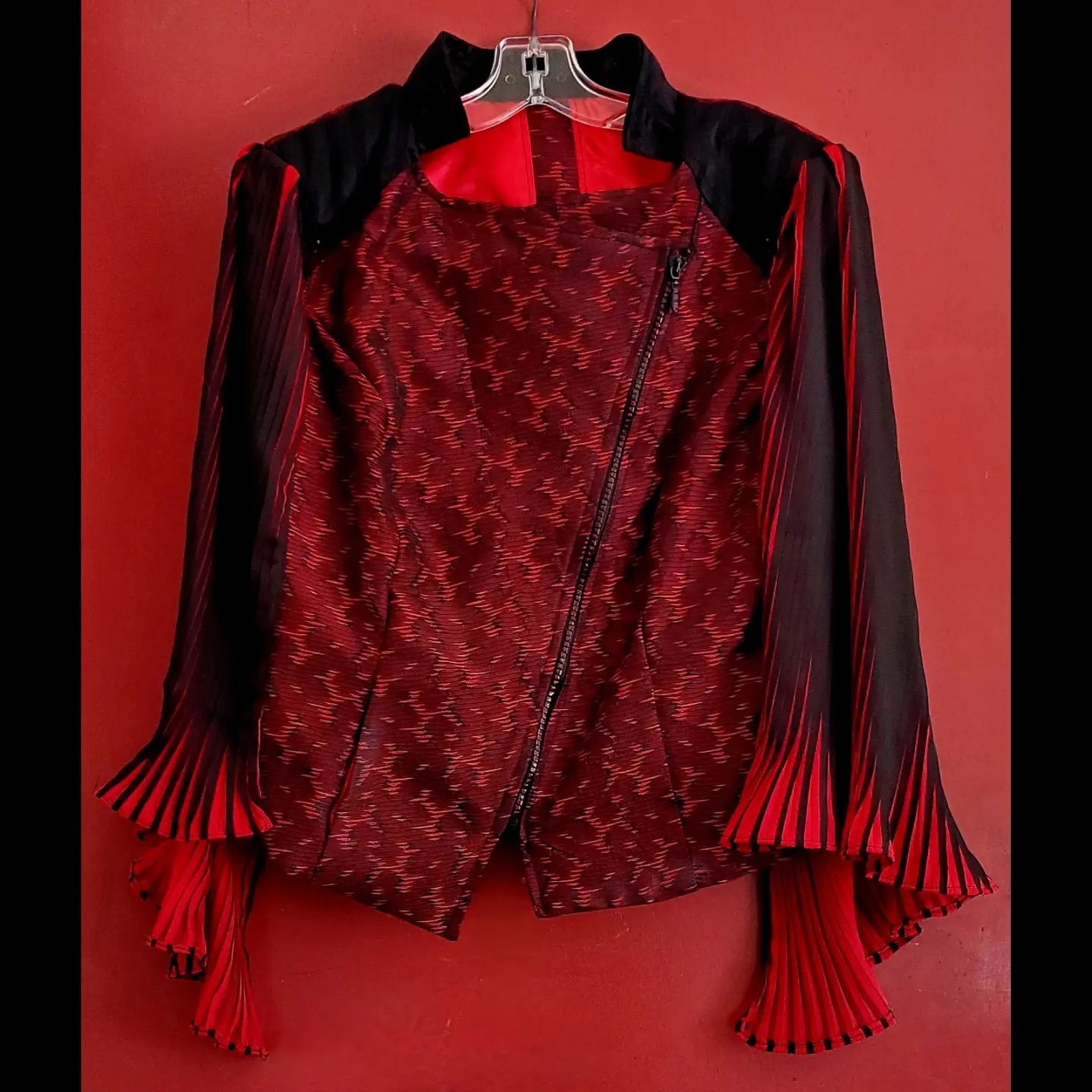 front view of red and black moto jacket with pleated cape sleeves and ruby rhinestone zipper fully zipped