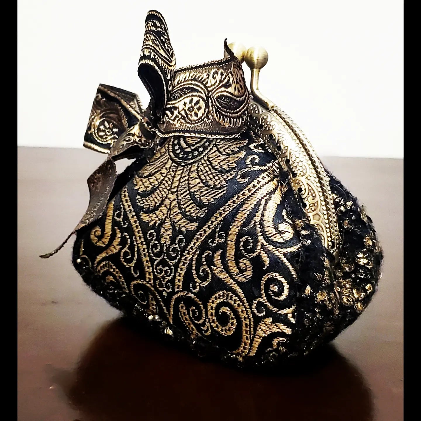 Side view of platinum and black paisley brocade coin purse with matching paisley bow accent