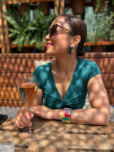 Model wearing green and gold button earrings drinking champagne