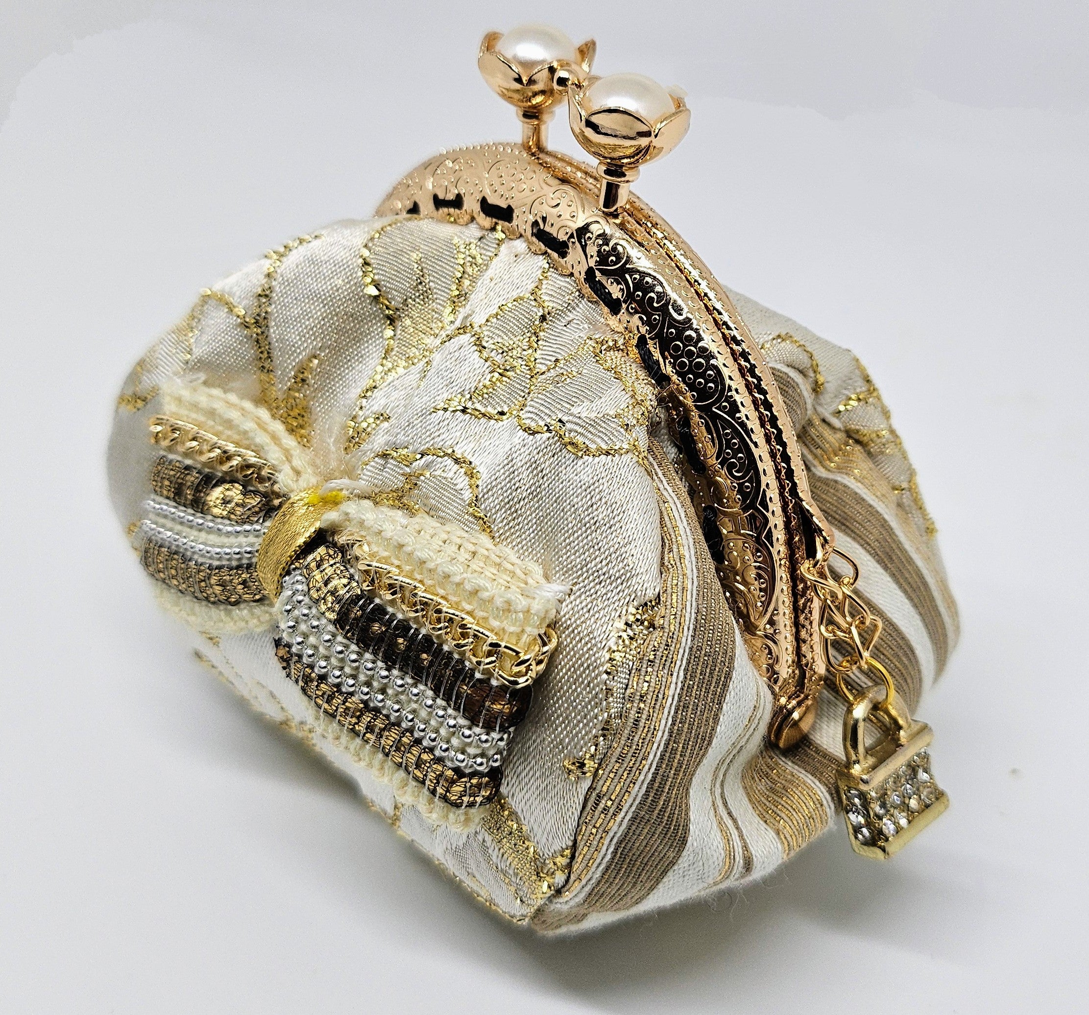 Side view of  Ivory and gold floral brocade kiss clasp coin purse with sequin and chain bow and ornate jeweled padlock charm