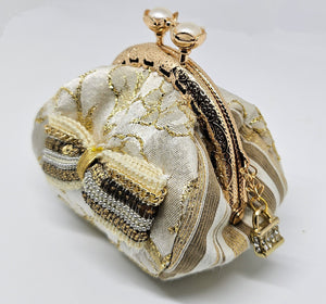 Side view of  Ivory and gold floral brocade kiss clasp coin purse with sequin and chain bow and ornate jeweled padlock charm