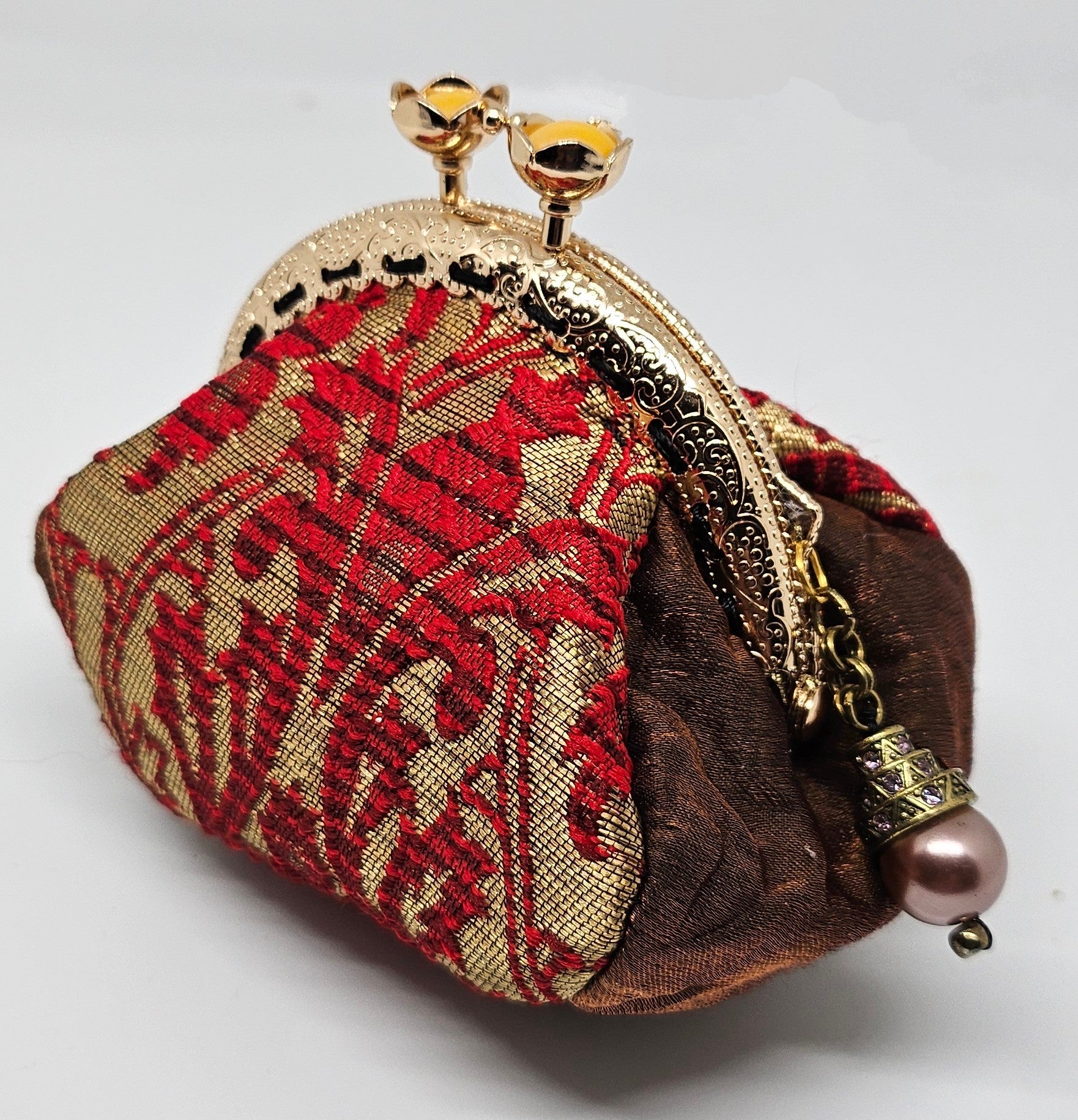 Side view of  Baroque print kiss clasp coin purse with ornate jeweled pearl charm. 