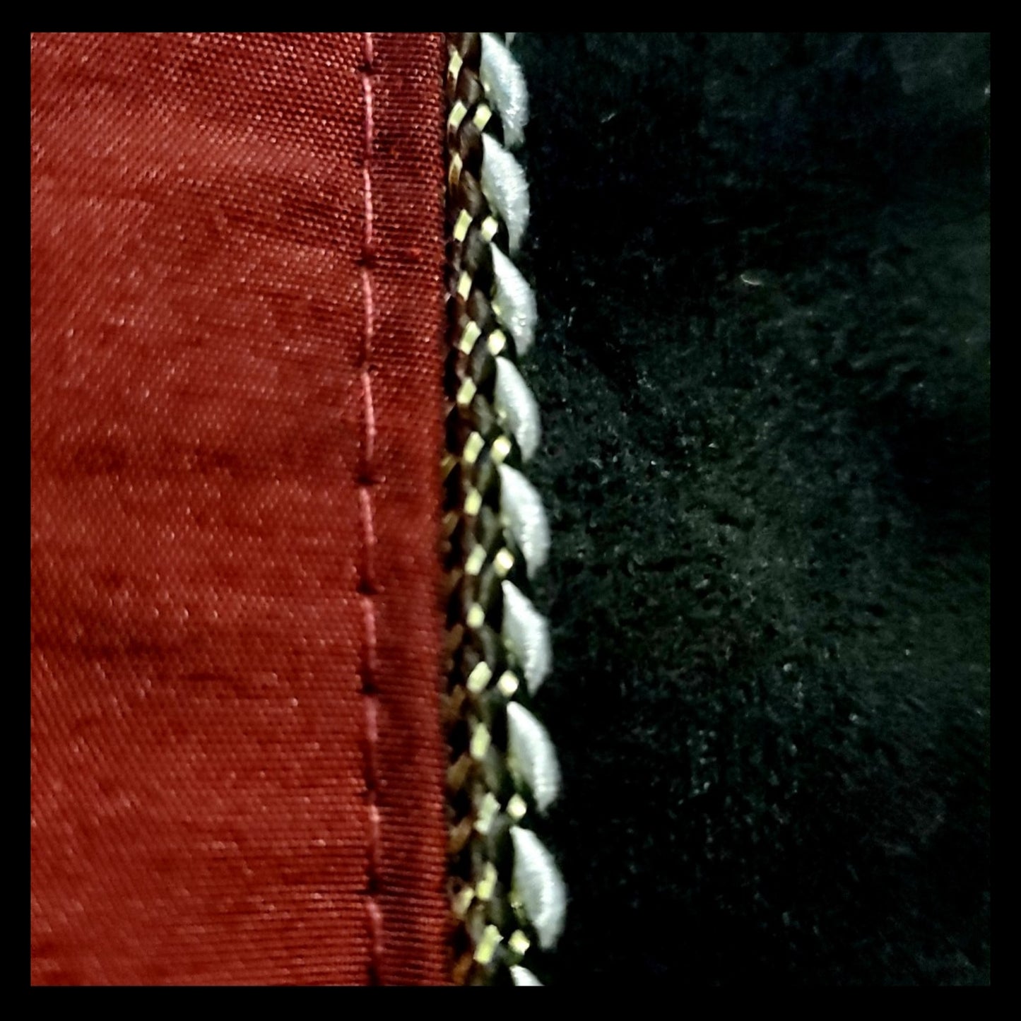 Close up view of fabric and piping of red taffeta and black velveteen colour-blocked bomber jacket with white cord piping