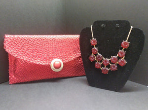 Front view of red clutch handbag styled with jewelry on black stand