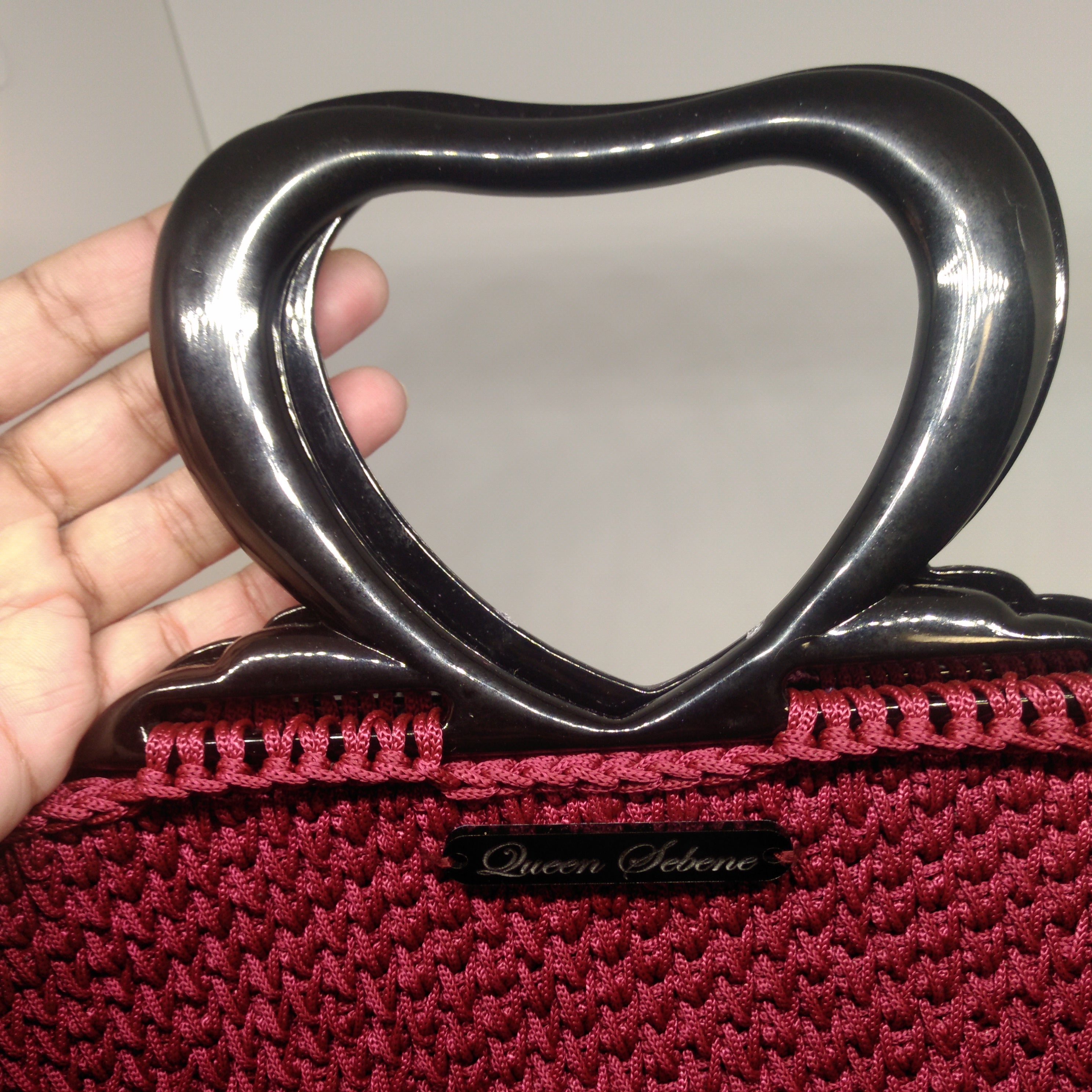 close up view of the handle of  Burgundy crochet handbag with black heart shaped acrylic handle