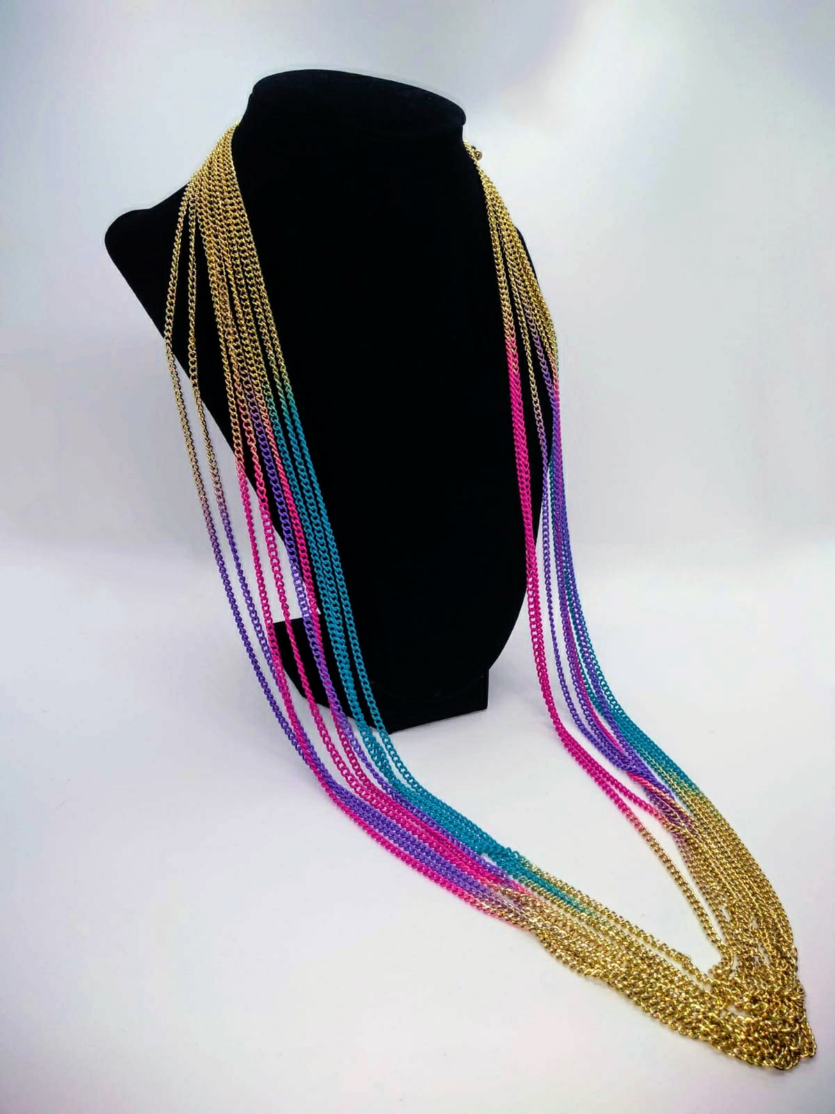 gold multi strand necklace with purple, turquoise, and pink accents draped on black stand