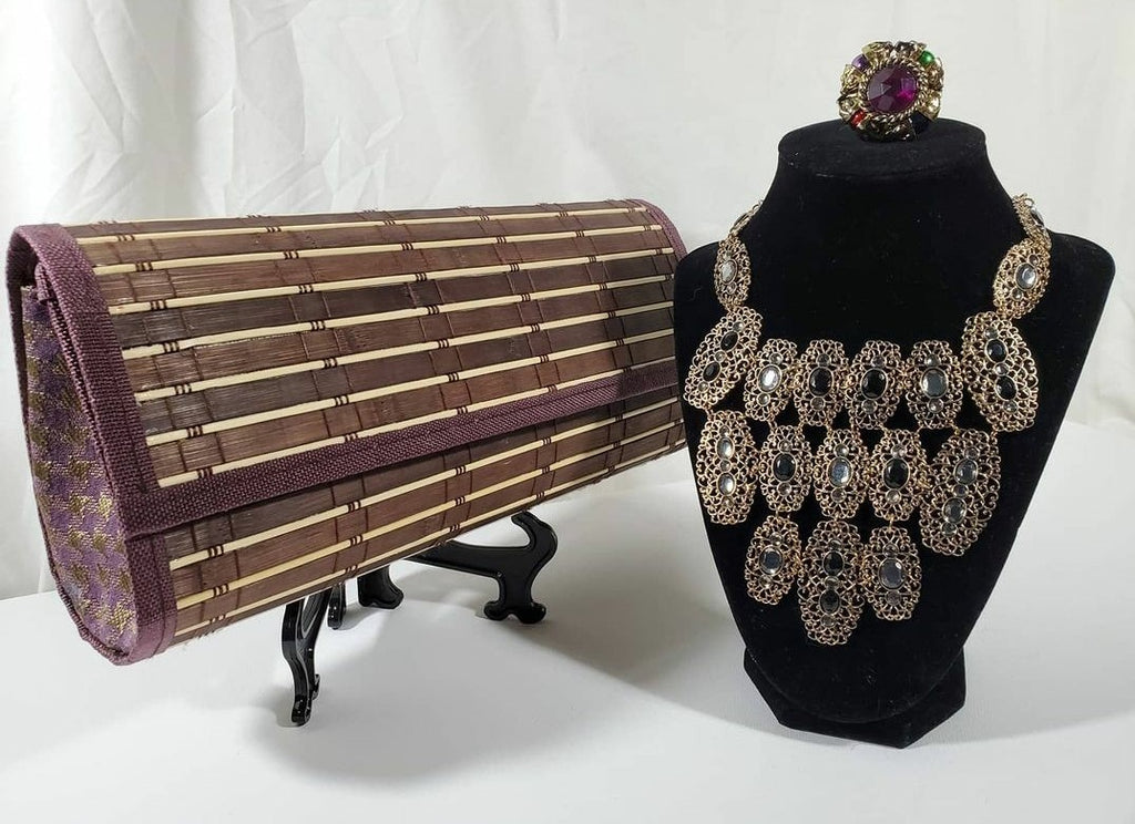 brown and purple wood clutch with brass and rhinestone chunky necklace on stand topped with beaded ring 