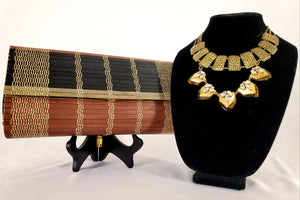 Striped wood clutch displayed with gold necklaces on jewelry stand.